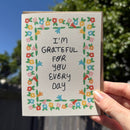 Hand holding a card with floral border and text 'I'm grateful for you every day'